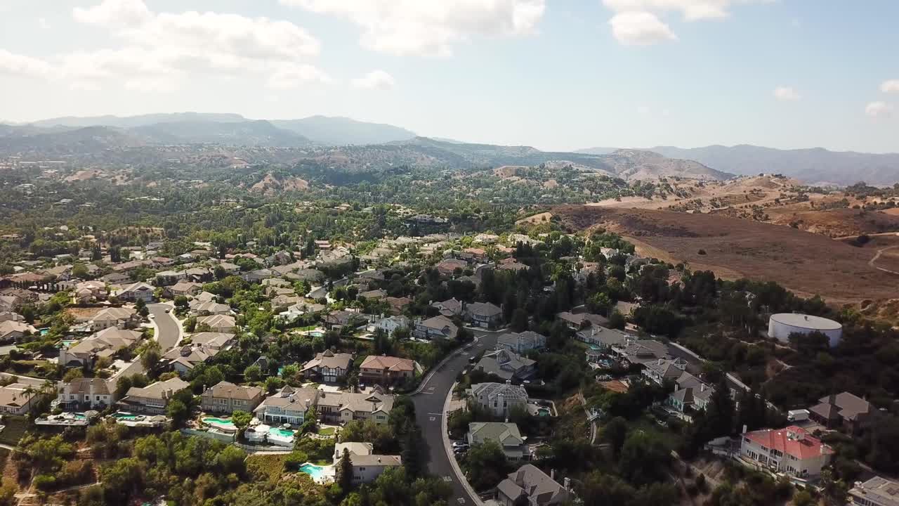 Aerial establishing shot of Hidden Hills Neighborhood with luxury homes and houses. Main street with driving cars and dry sandy desert mountains in California. Sunny day in USA. Wide shot.