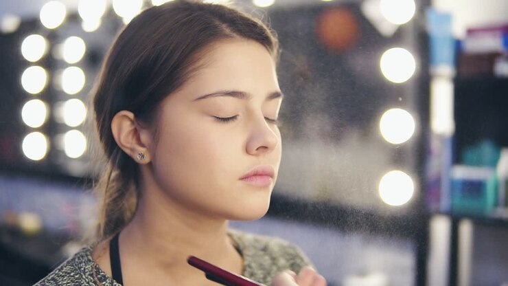 Professional makeup artist fixing young woman's makeup with spray in a beauty salon. Slow Motion shot: Spray sprinkles on the