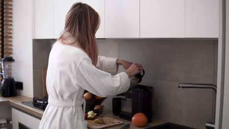 woman in white robe making apple or pear juice in the morning using juicer at kitchen