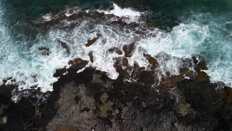 Vista-Ascendente-Hacia-Abajo-De-Una-Costa-Volcánica-Con-Las-Olas-Rompiendo-Contra-Las-Rocas