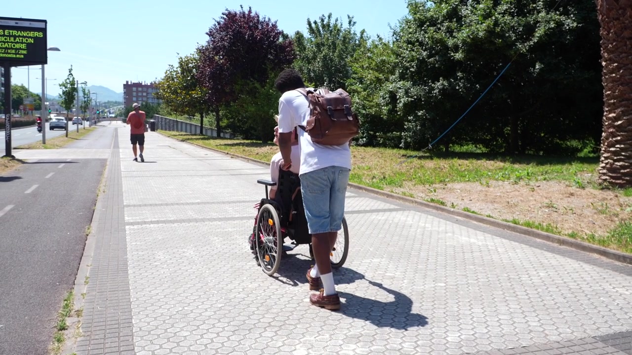 Young Man Pushing Senior Woman in Wheelchair Along City Sidewalk