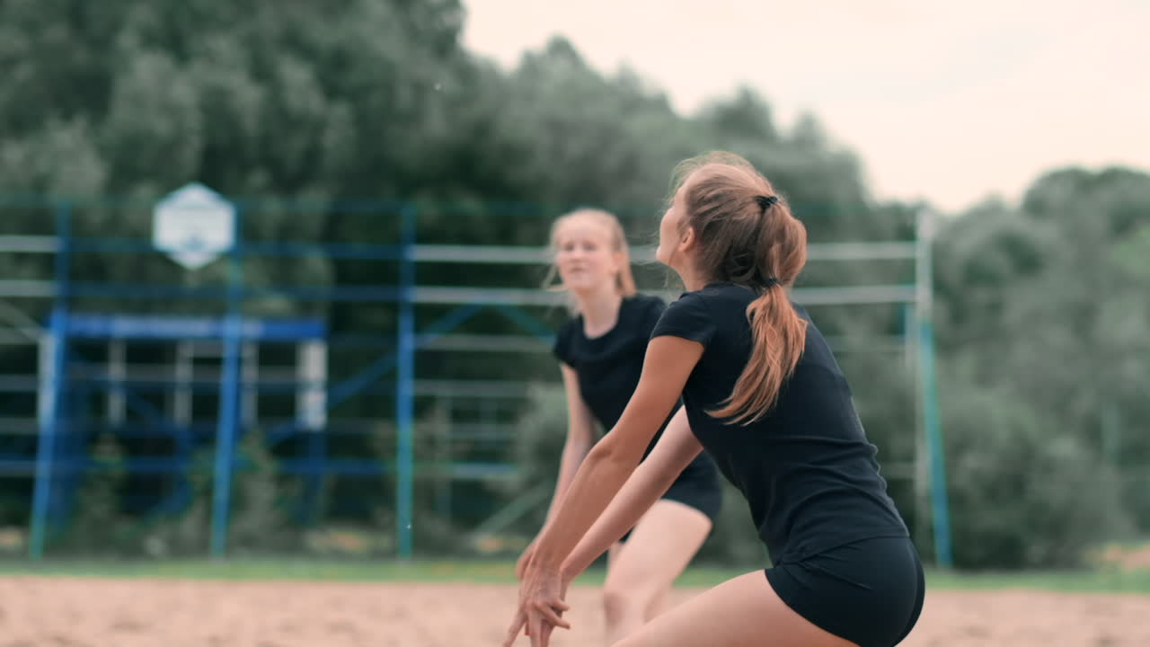 Nuori nainen pelaa lentopalloa rannalla joukkueessa, hyökäten ja lyöden palloa. Hidastettuna tyttö lyö pallon verkon yli hyökkäyksenä.