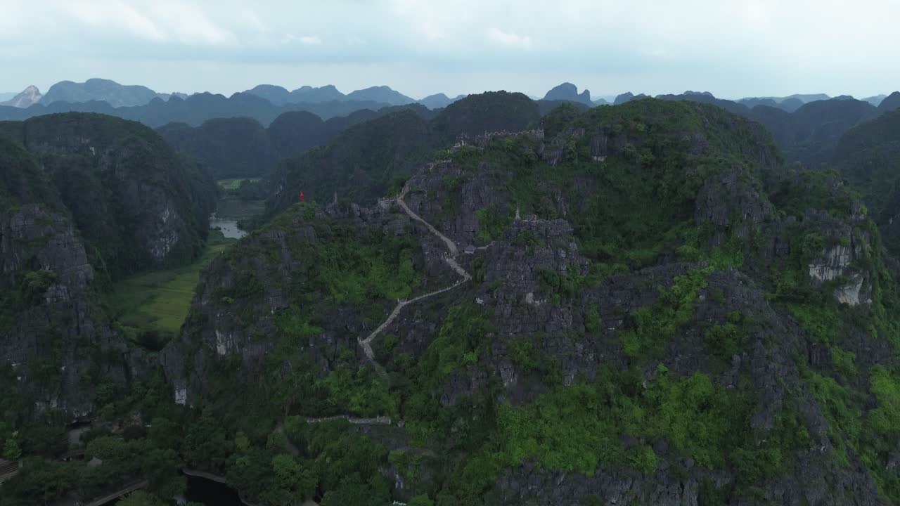 Camera lifting from lotus ponds and trees up to rocky limestone cliffs in lush Ninh Binh region