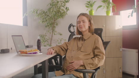 Mujer-Embarazada-Trabajadora-Sentada-En-El-Escritorio-Y-Sonriendo-A-La-Cámara-Durante-El-Almuerzo-De-Oficina-1