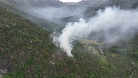 Forest-wildfire-just-started-in-green-and-dry-mountain-hillside---Slowly-rotating-aerial-showing-smoke-pouring-up-in-the-air