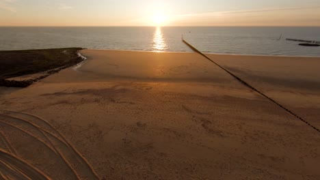 Drone-flying-behind-the-dunes-revealing-a-beautiful-sunset-on-a-deserted-beach