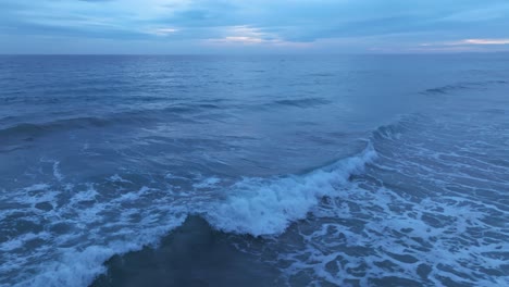 Primer-Plano-Sobre-Las-Olas-Del-Océano-Volando-Desde-Los-Lados-Con-Vista-Al-Atardecer-En-El-Horizonte-En-Menorca-España