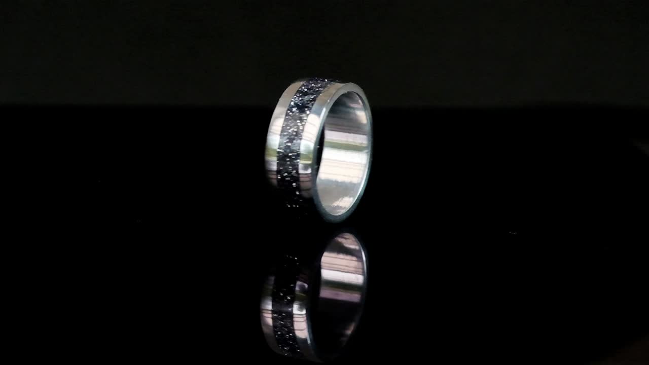 A hand crafted ring made of steel and epoxy spinning on a reflective surface
