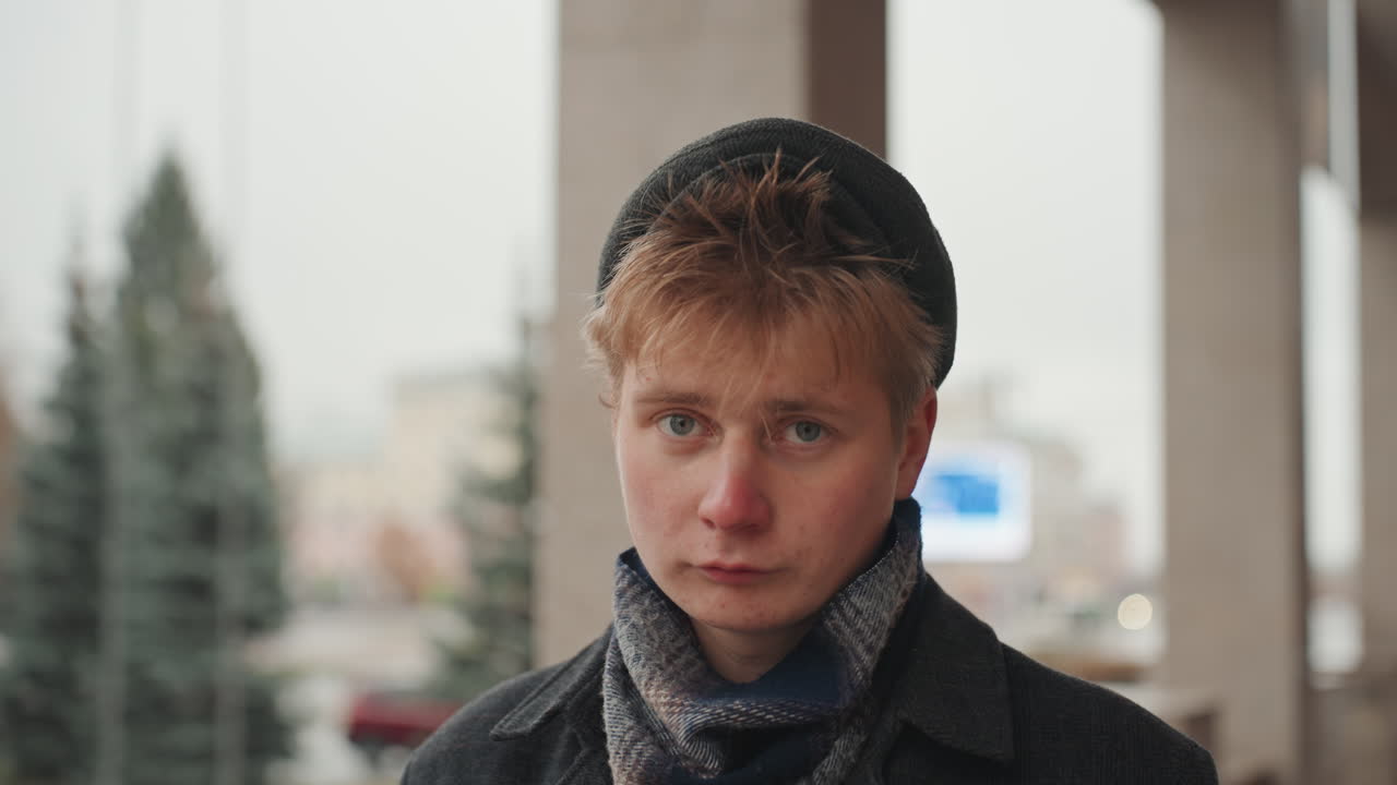 Youthful filmmaker admires cityscape. Male young director watches nighttime city scene. Young male filmmaker dressed for cold weather thoughtfully observing glowing city lights from porch