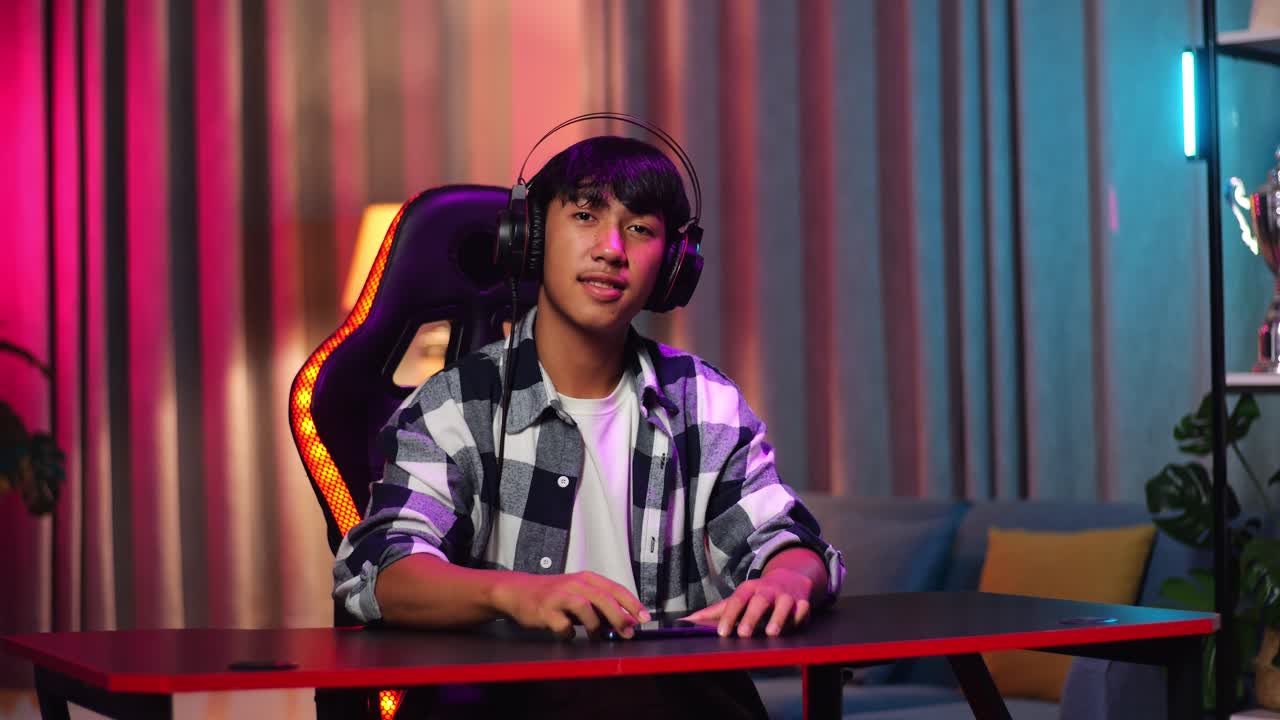 Ragazzo adolescente asiatico gamer che sorride alla telecamera con le braccia incrociate mentre gioca a un videogioco sullo smartphone
