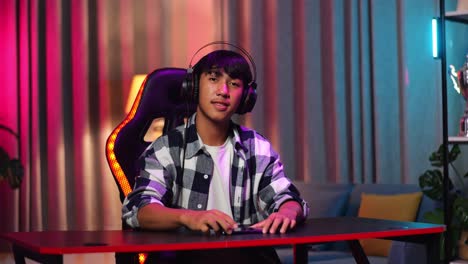 un adolescente asiático sonriendo a la cámara con los brazos cruzados mientras juega videojuegos en su teléfono inteligente