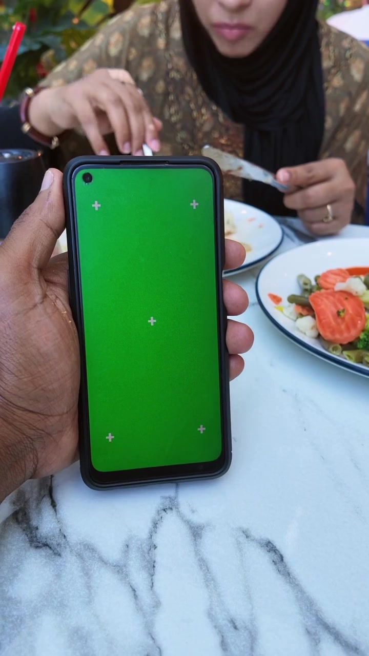 Person Holding Smartphone with Green Screen at Restaurant Table