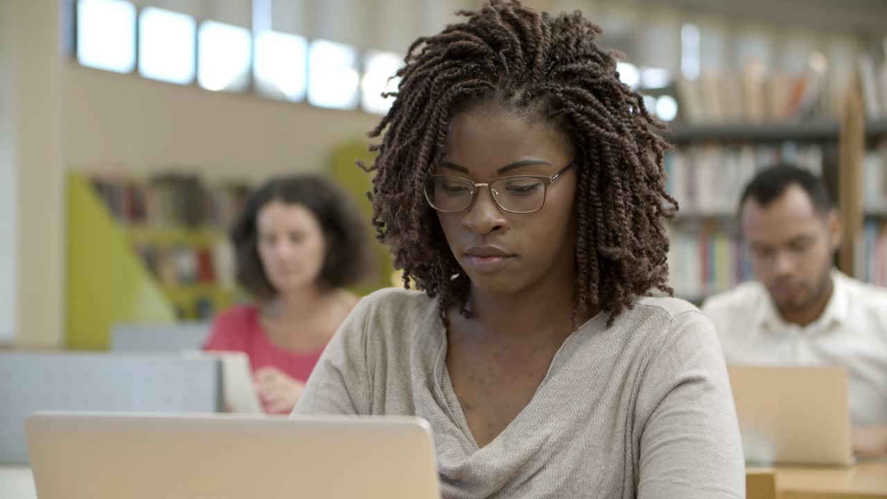 estudiante pensativo que trabaja con un dispositivo moderno en la biblioteca pública