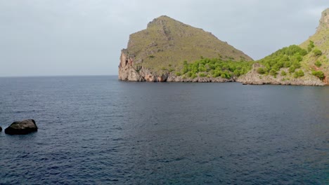 Reveal-shot-of-a-massive-rocky-cliff-of-island-in-the-surrounding-sea-water,-aerial-view