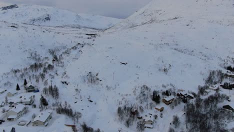 Drone-view-in-Tromso-area-in-winter-flying-over-a-small-town-with-a-full-of-snow-landscape-and-white-mountains-next-to-a-fjord-in-Norway