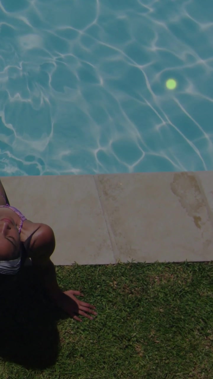 Sitting woman shifting back at backyard pool, showing swim top straps and particles, copy space