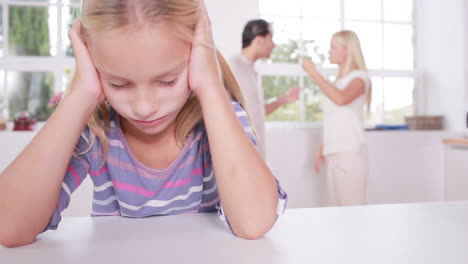 little girl looking depressed in front of fighting parents