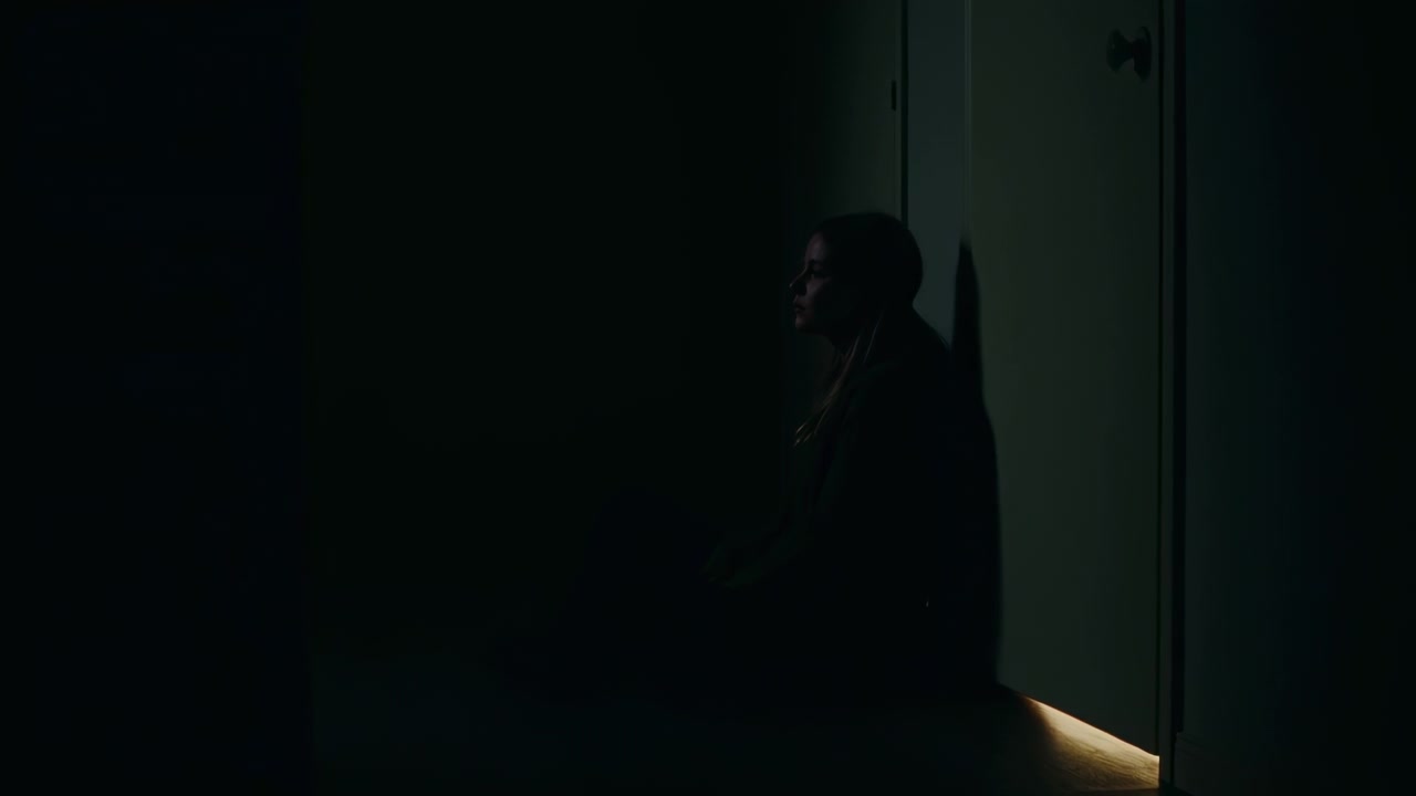 Jovem Mulher Sentada Sozinha em Quarto Escuro com uma Fresta de Luz Debaixo da Porta