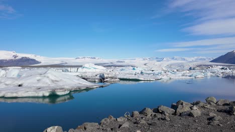 witness the tranquil beauty of iceland's winter wonderland, where two ducks glide effortlessly on a river, surrounded by snow-covered mountains and a dynamic sky