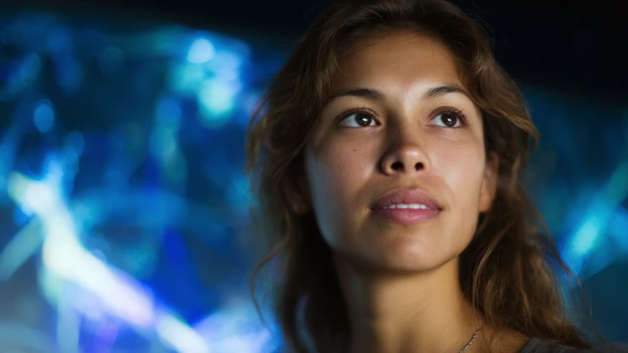 A contemplative moment of a young woman gazing upwards, illuminated softly against a backdrop of vibrant blue and abstract lights, reflecting curiosity and wonder in her expression while captured beautifully in close-up frames