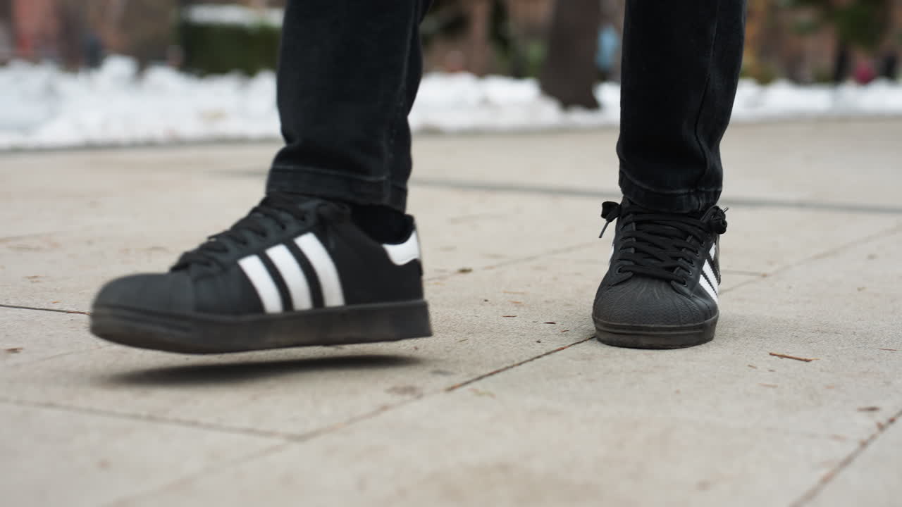 검은색 바지와 스니커를 입은 사람이  줄무로 은 길을 고 있는 모습, 눈과 나무가 있는 흐릿한 배경