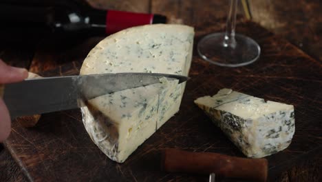 mano masculina con un cuchillo corta un pedazo de queso brie.