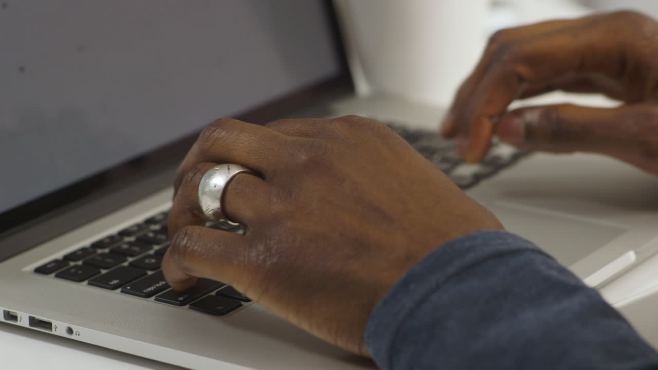 A close up of an African-American man's hands as he types on a MacBook Pro laptop in an office