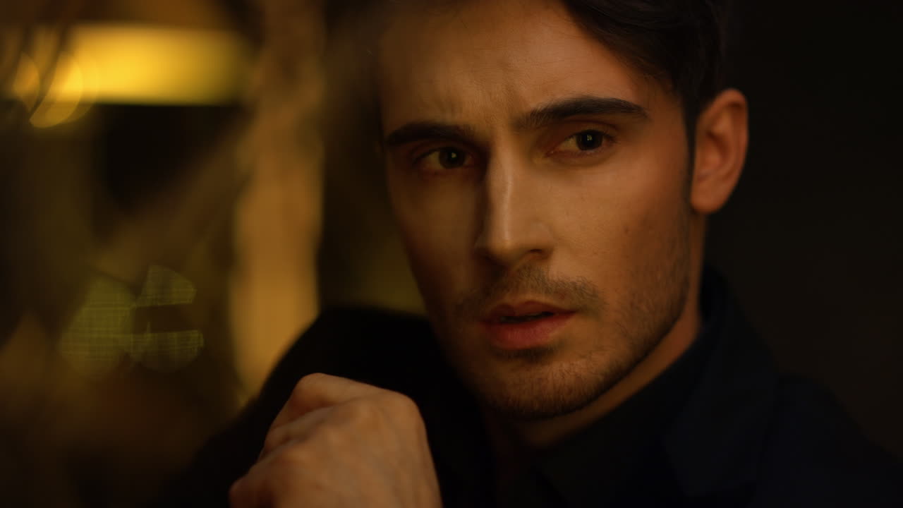 섹시한 남자의 얼굴이 어두운 방에서 무언가를 보고 부자가 실내에서 얼굴을 만지고 있습니다.