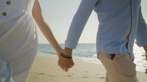 cropped shot of couple holding hands and walking on beach