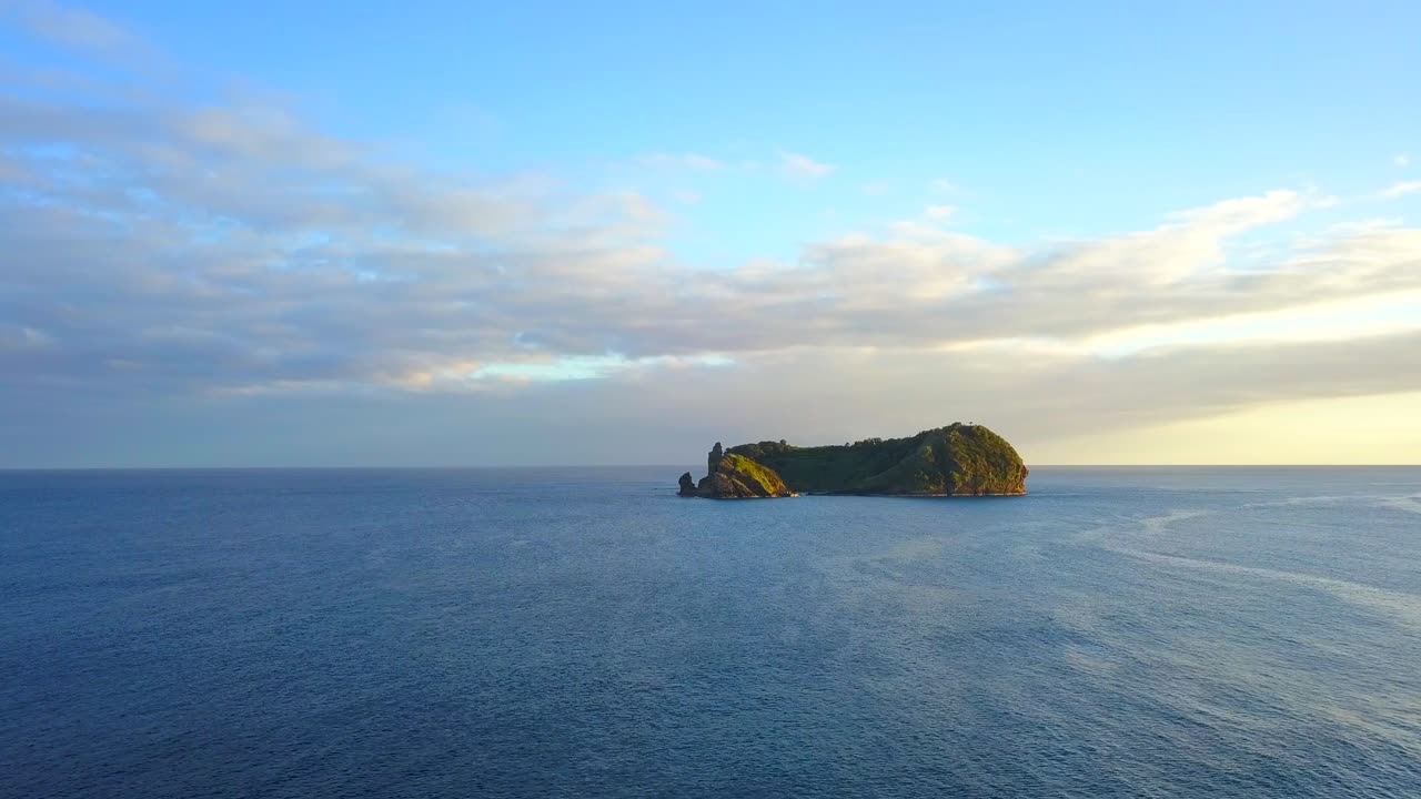 Drone flying towards tropical island in middle of blue ocean at sunset. Tourism in Azores