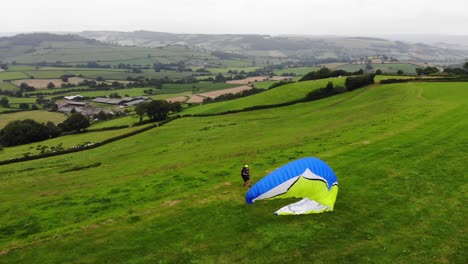 parallax view of a paraglider inflating his wing before take off with beautiful english countryside as a backdrop