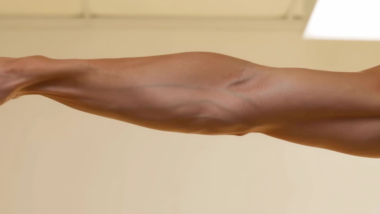 Vista laterale di un singolo avambraccio umano che si estende verso una presa verticale in un interno caldo beige, la mano si apre e poi si chiude attorno al bordo mentre il polso si raddrizza sotto una luce soffusa e diffusa, con braccio, avambraccio.