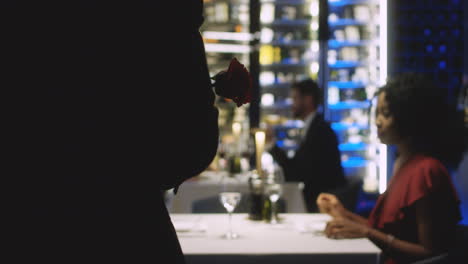 a man offering a red rose to his girlfriend in a restaurant