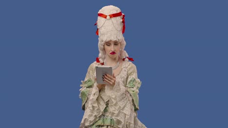 portrait of courtier lady in white vintage lace dress and wig is viewing information on a digital tablet. young woman posing in studio with blue screen background. close up. slow motion ready 59.94fps