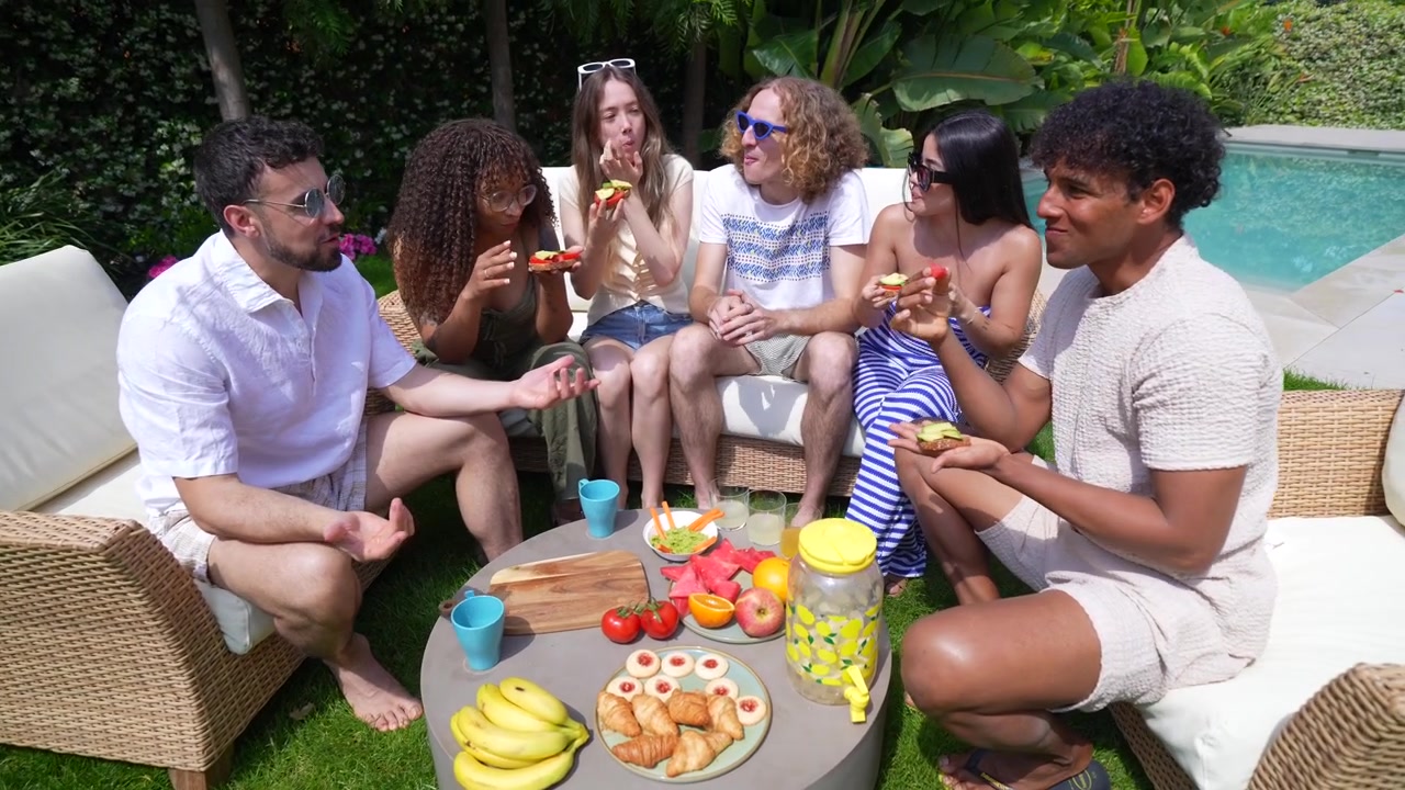 Diverse groep vrienden geniet van een buitenbrunch en gesprekken bij het zwembad.