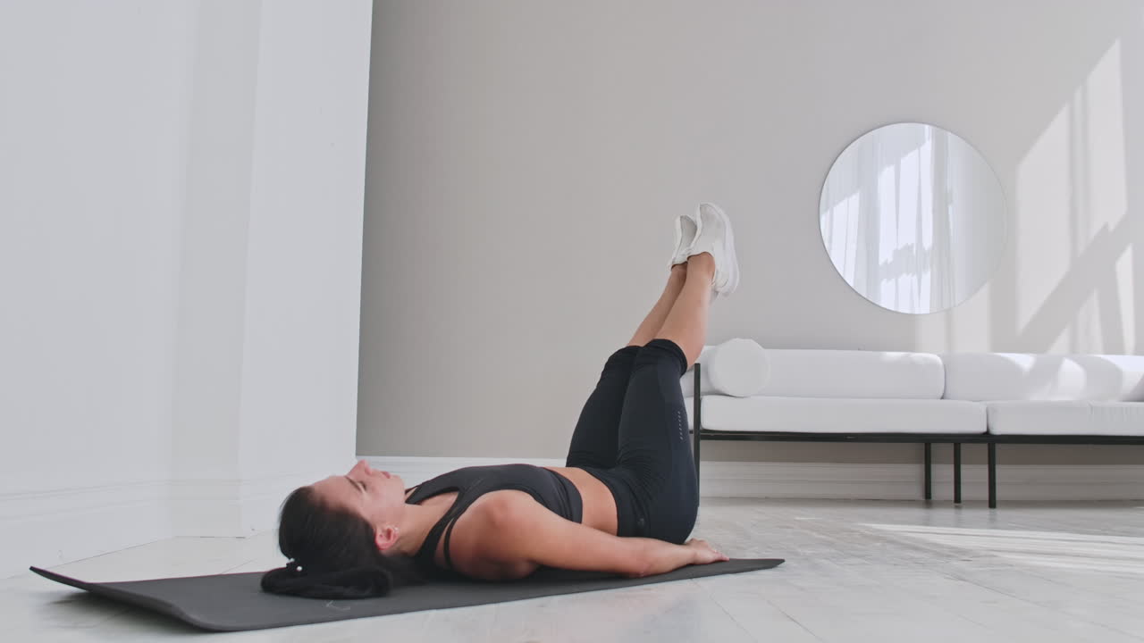 deportista entrenando en casa. atleta femenina en forma haciendo ejercicio de toque de dedo del pie con un solo brazo tendida en el suelo en un apartamento blanco.