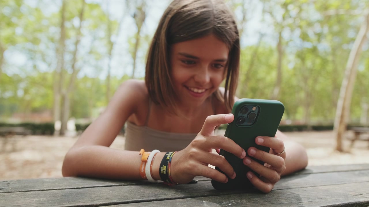 Ragazza sorridente che usa lo smartphone a un tavolo in un parco all'aperto