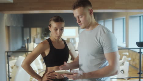 gym trainer using tablet and speaking with woman