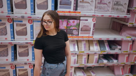 aerial view of lady shopping in store, walking past shelf with bedding products, she looks around while browsing different options, store aisle filled with neatly arranged home textiles and bed sets