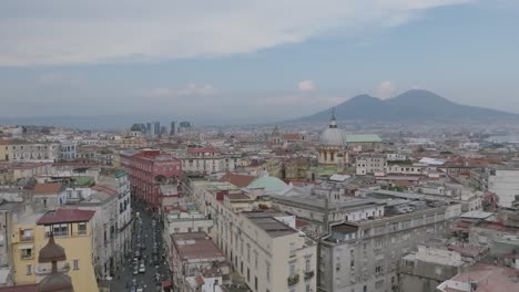 aerial video flying over buildings in naples, italy and focusing on the spire of a church with mount vesuvius in the background