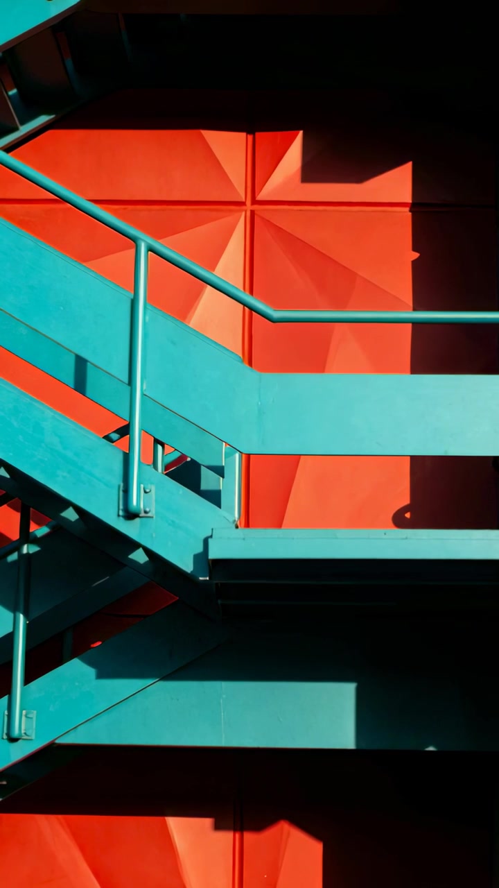 Video verticale: Telecamera che si sposta rivelando una scala metallica color verde acqua contro un rivestimento rosso, studiando la luce.
