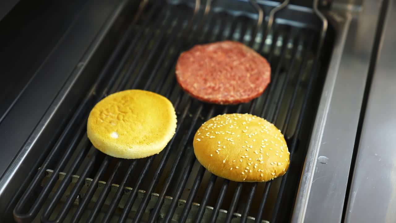 Two burger buns and one cutlet are being cooked on a barbecue grill. Delicious homemade burger.