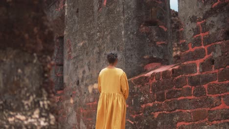 Woman-in-a-yellow-dress-stands-in-front-of-ancient-red-brick-ruins