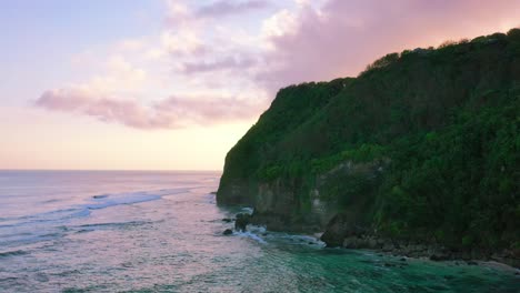 aerial of beautiful calm ocean waves crashing onto uluwatu cliffs with pink and purple sky