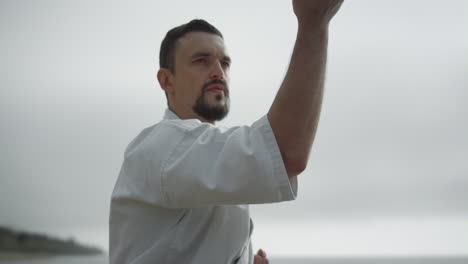 Karate-man-making-hands-exercises-practicing-martial-arts-on-beach-close-up.