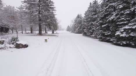 Icy-town-street-during-snowfall,-low-angle-drone-dolly-forward-view