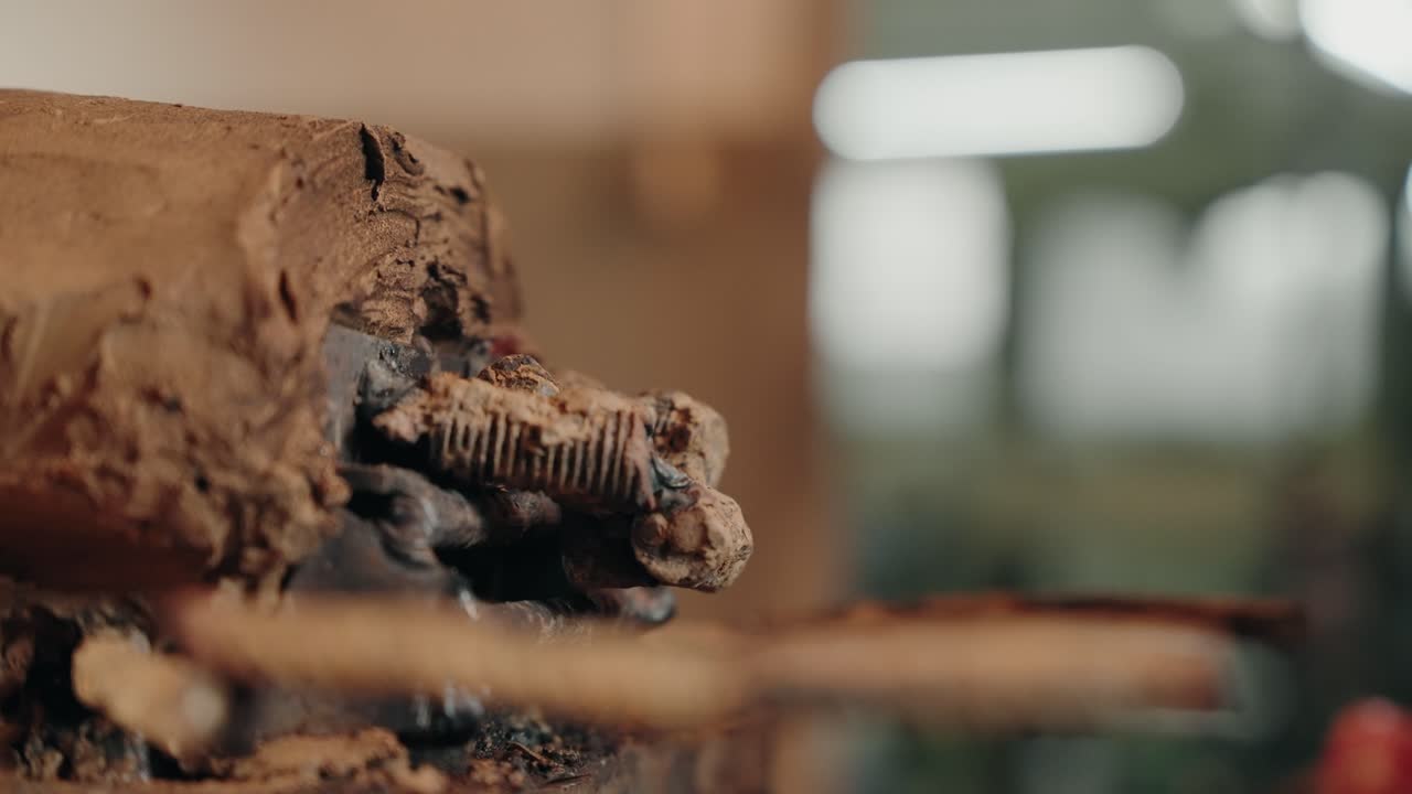 Gloved hands welding metal in clay mold sculpture workshop setting