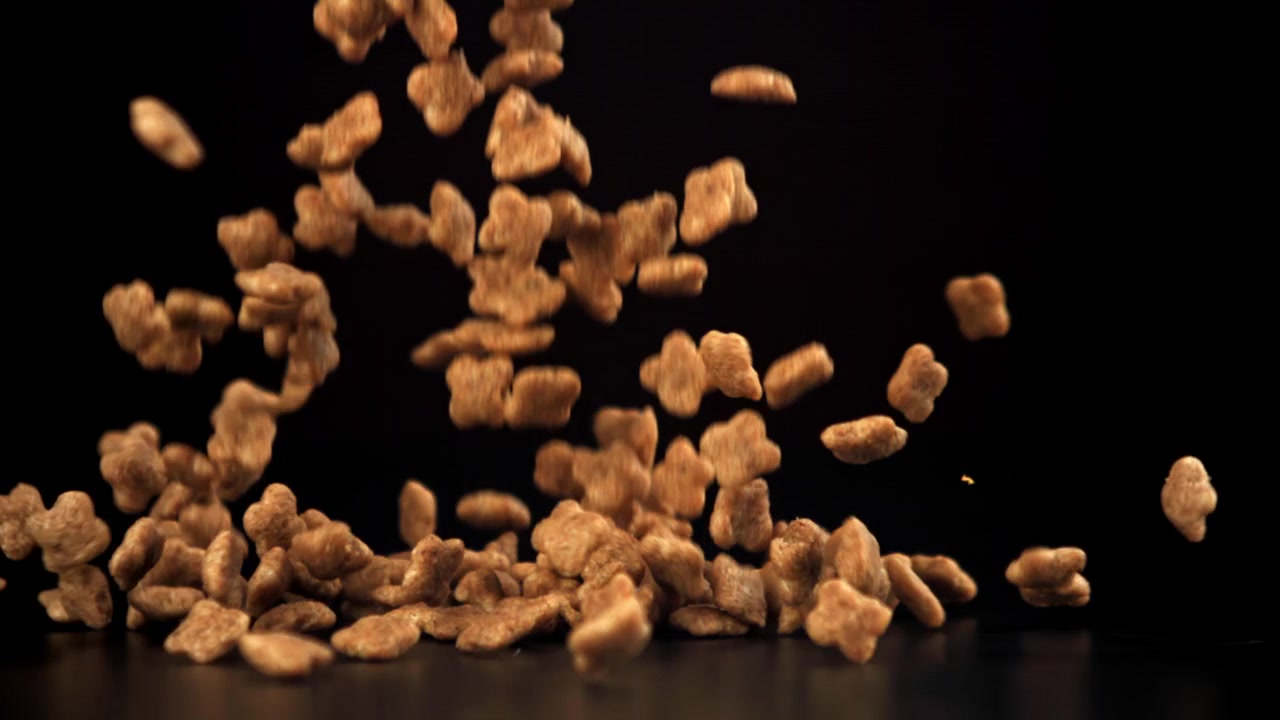 Trockenfutter-Kroketten fallen in Zeitlupe auf schwarzem Hintergrund