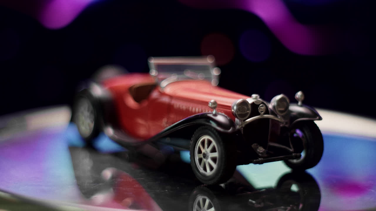 A red vintage toy car reflecting on a shiny surface with colorful bokeh lights