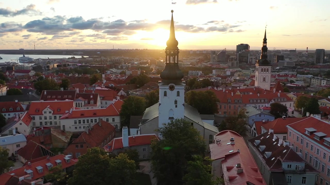 Filmato mozzafiato con drone del Centro Storico medievale di Tallinn al tramonto. L'inquadratura mostra la Collina di Toompea, la Cattedrale di Santa Maria e gli edifici dai tetti rossi sotto un cielo drammatico di nuvole rosa e arancioni.